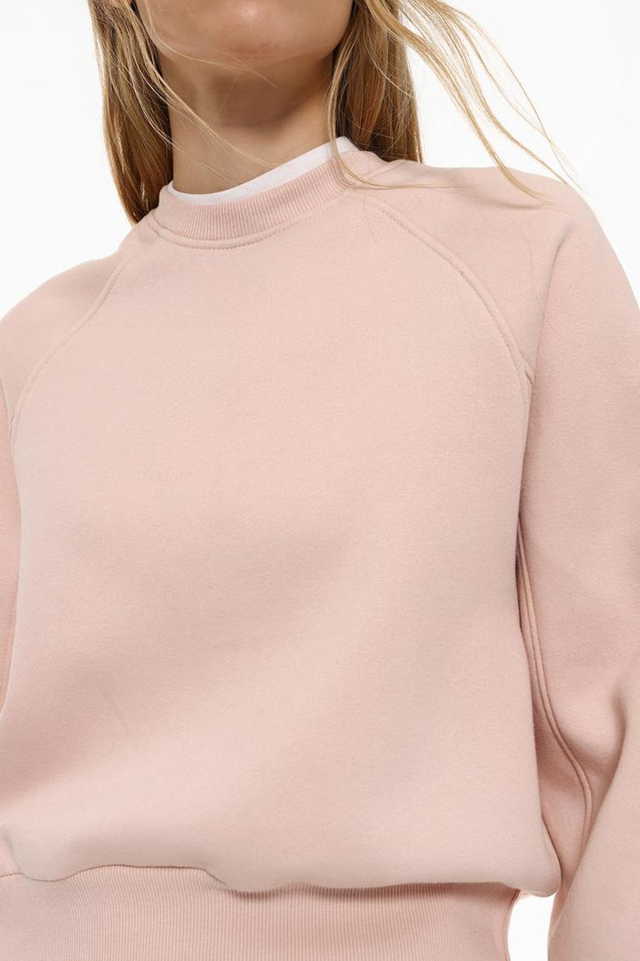 Zoomed-in view of the body of a women's pink basic cropped sweatshirt, highlighting the fabric texture, stitching, and cropped design details.