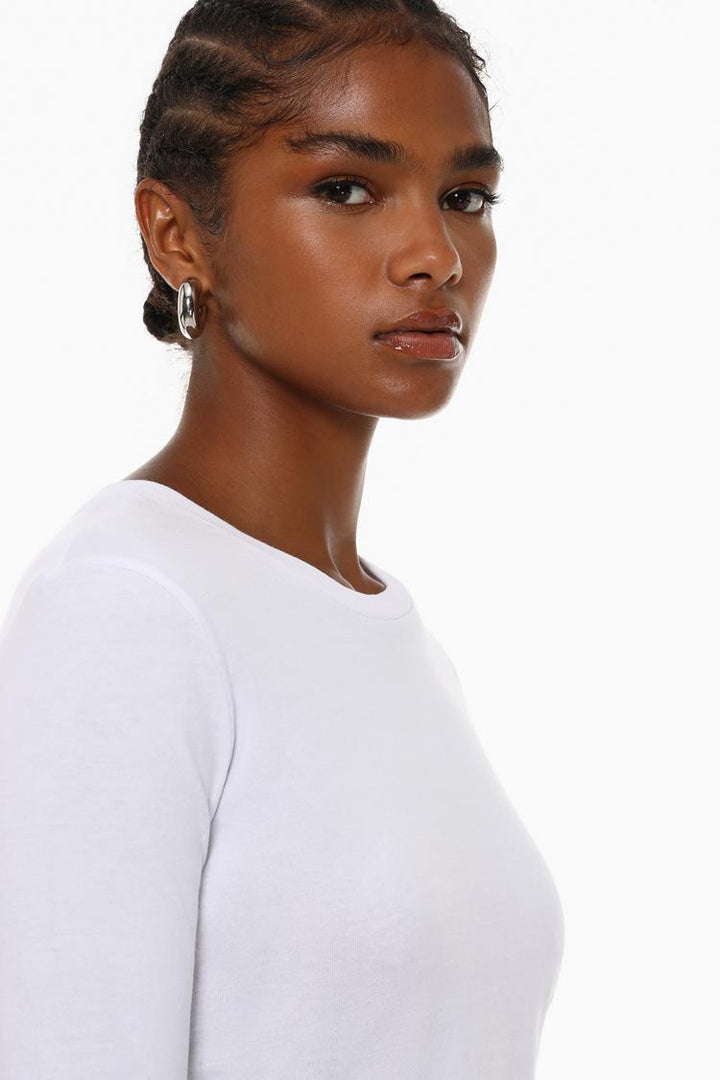 Model wearing the white cropped long-sleeve top, showcasing its sleek design, long sleeves, and cropped fit for a chic, casual look. Perfect for creating a stylish, effortless outfit.