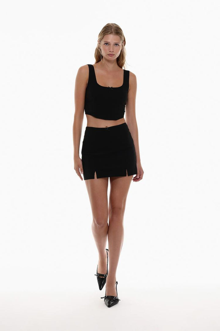 Body view of the black rustic strappy top with a bow worn by a model, showcasing the delicate straps and playful bow detail for a chic, feminine look that flatters the figure.