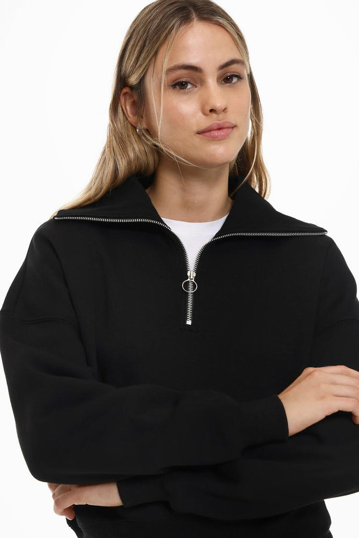 Body view of a women's black sweatshirt with a zip-up collar, showcasing the relaxed fit and versatile design.