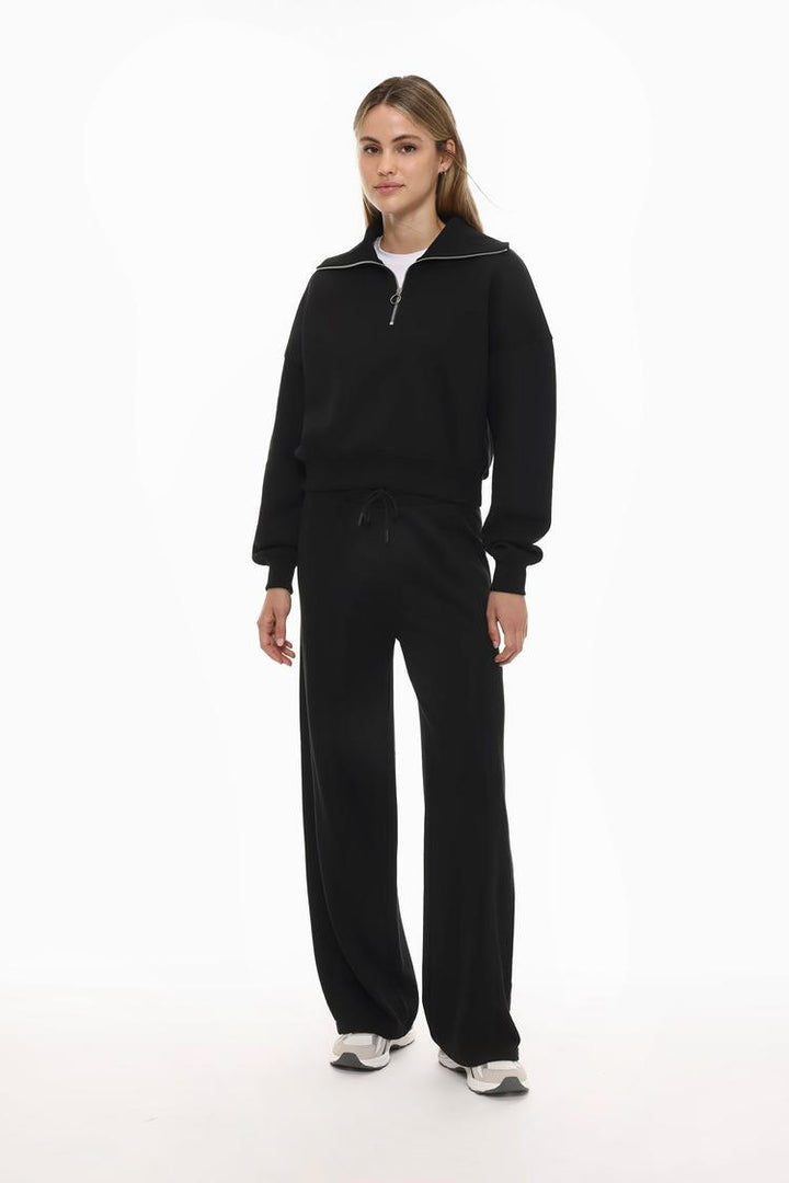 Full-body view of a women's black sweatshirt with a zip-up collar, styled for a casual and comfortable look.