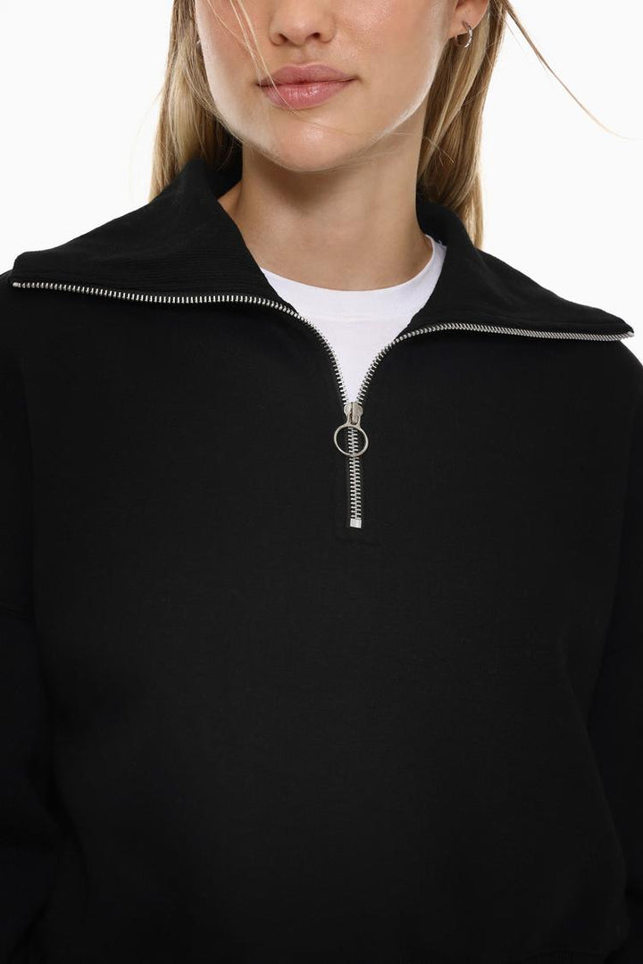 Zoomed-in view of a women's black sweatshirt with a zip-up collar, highlighting the fabric texture, zipper details, and stitching.