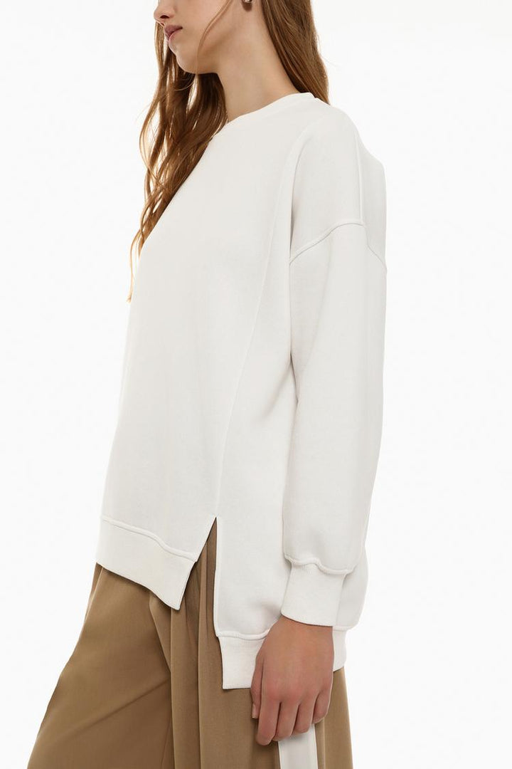 Zoomed-in side view of a women's white oversized sweatshirt, highlighting the asymmetric design and fabric details.