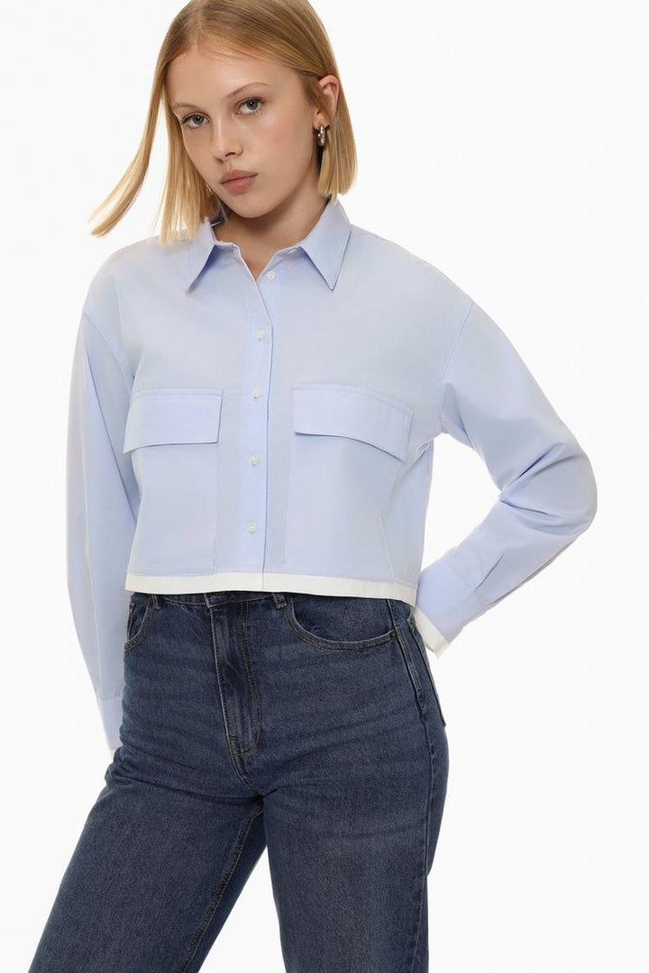 A full-body view of the contrast cropped shirt, displaying its stylish design. The shirt typically features contrasting elements such as different colors, textures, or patterns, giving it a modern, edgy look. This view captures the shirt's cropped length, highlighting its fashion-forward and casual appeal.