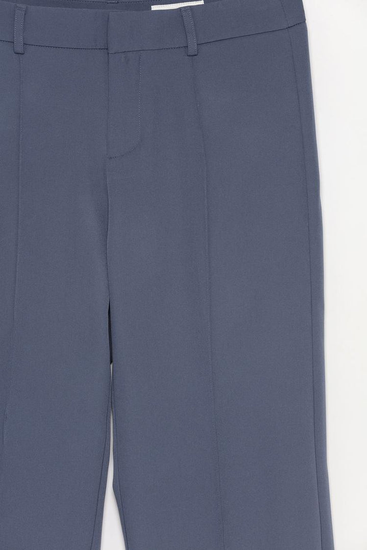 Close-up shot of the blue flared trousers with pleats, highlighting the pleating design and the fabric's texture.