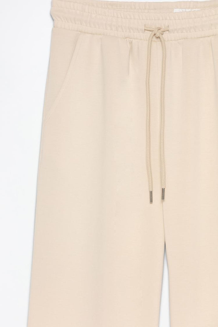 Product view of beige flowing sports trousers featuring the fabric and details.