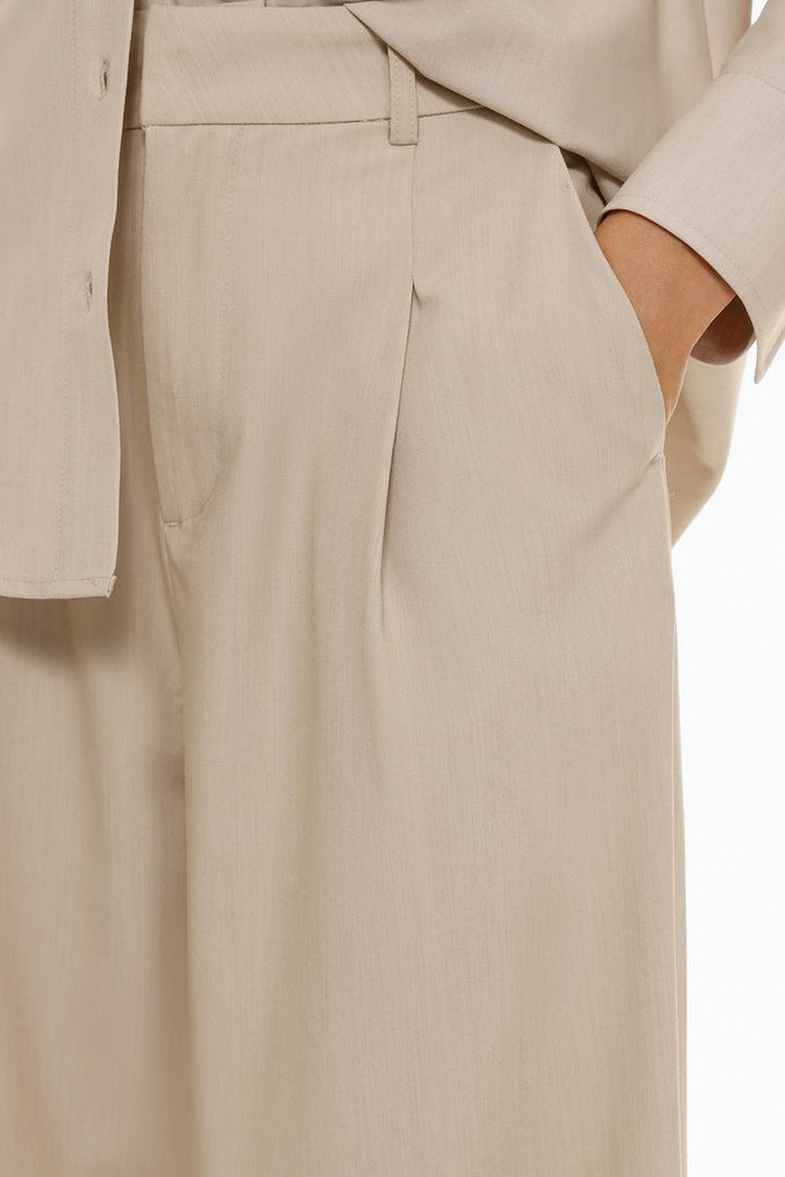 Loose-fitting beige wide-leg trousers, offering a chic and relaxed vibe