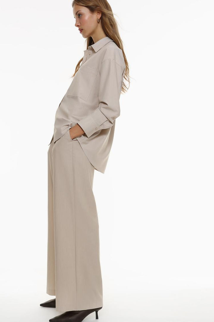 Side view of loose-fitting beige wide-leg trousers, emphasizing the flowy design and comfort