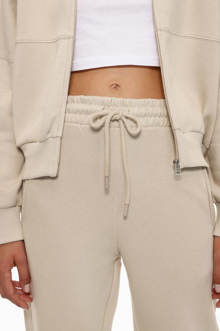 Body shot featuring the beige oversized tracksuit trousers, showing the full length and casual vibe of the trousers.