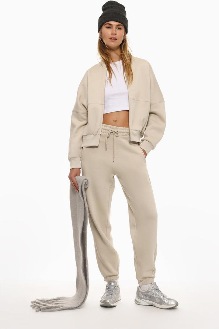 Full-body image of someone wearing beige oversized tracksuit trousers, styled as part of a full outfit.