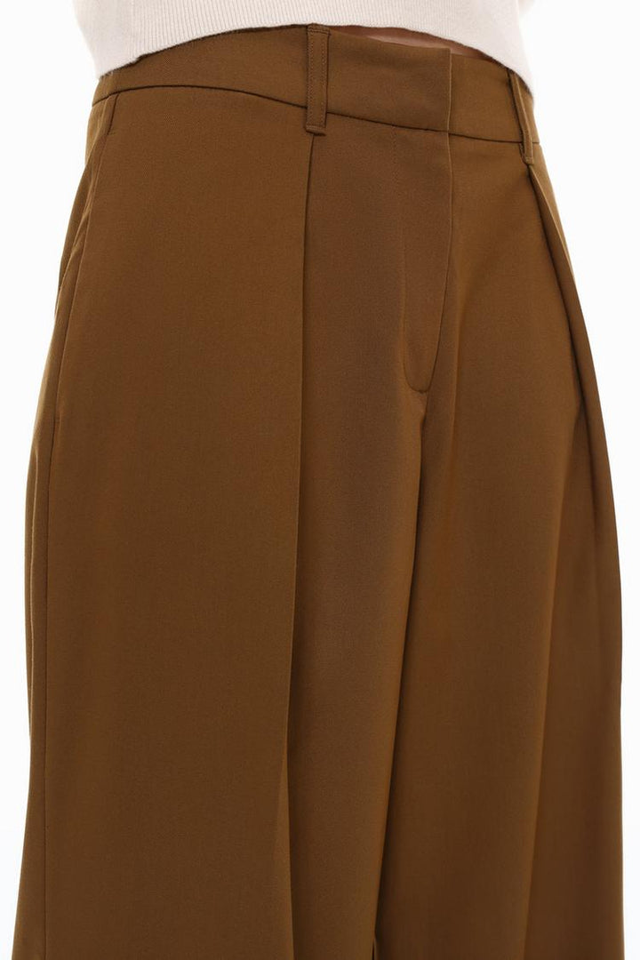 Close-up image of the brown pleated wide-leg trousers, focusing on the pleats, stitching, and fabric texture.