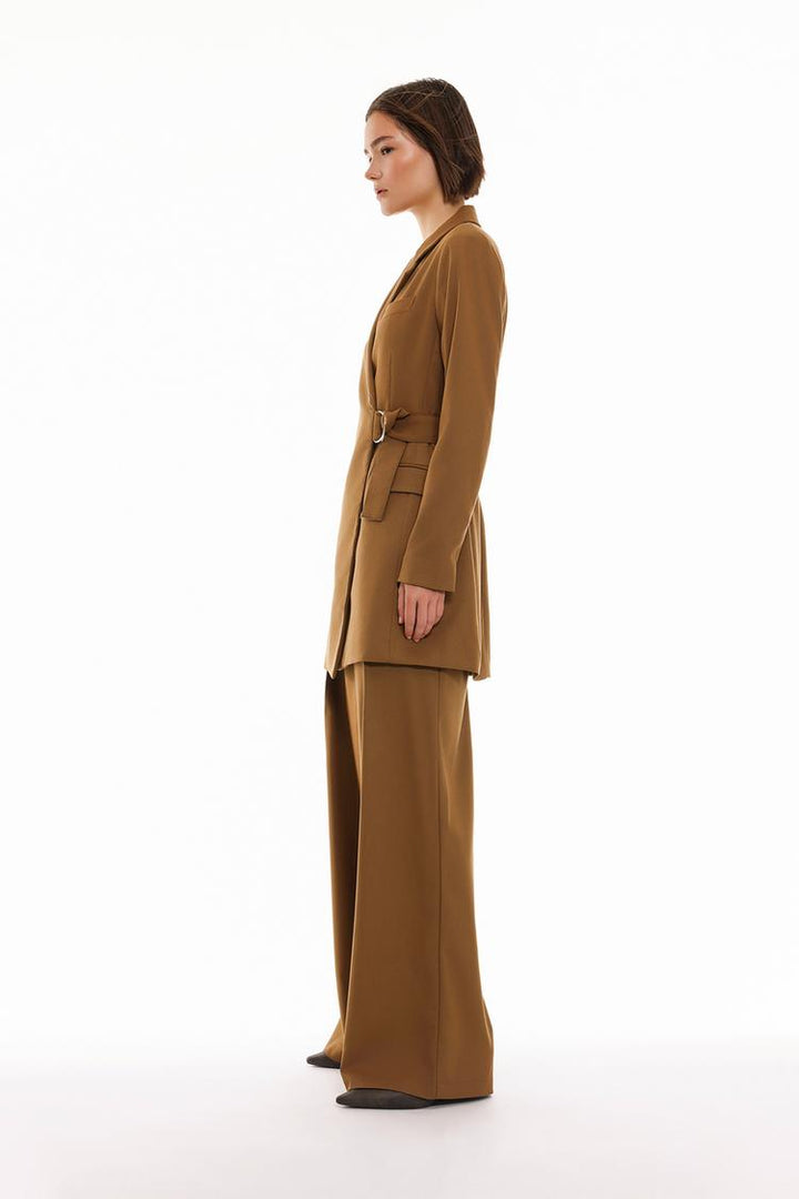 Side view of the brown pleated wide-leg trousers, showing the length and pleats from the side, as well as the overall relaxed silhouette.