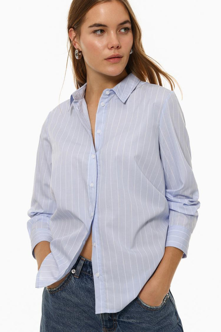 Model wearing a blue poplin shirt, highlighting the shirt's fitted design and smooth fabric, with a professional and sleek look.