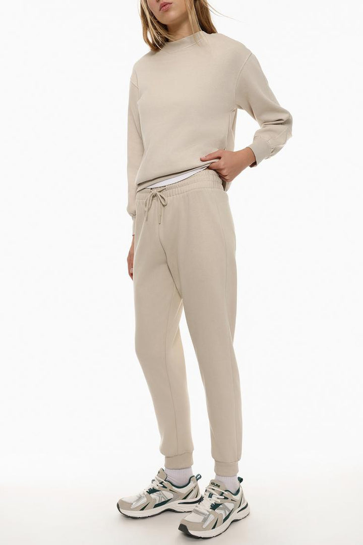 Side body view of beige tracksuit bottoms worn on a model for sizing and fit.