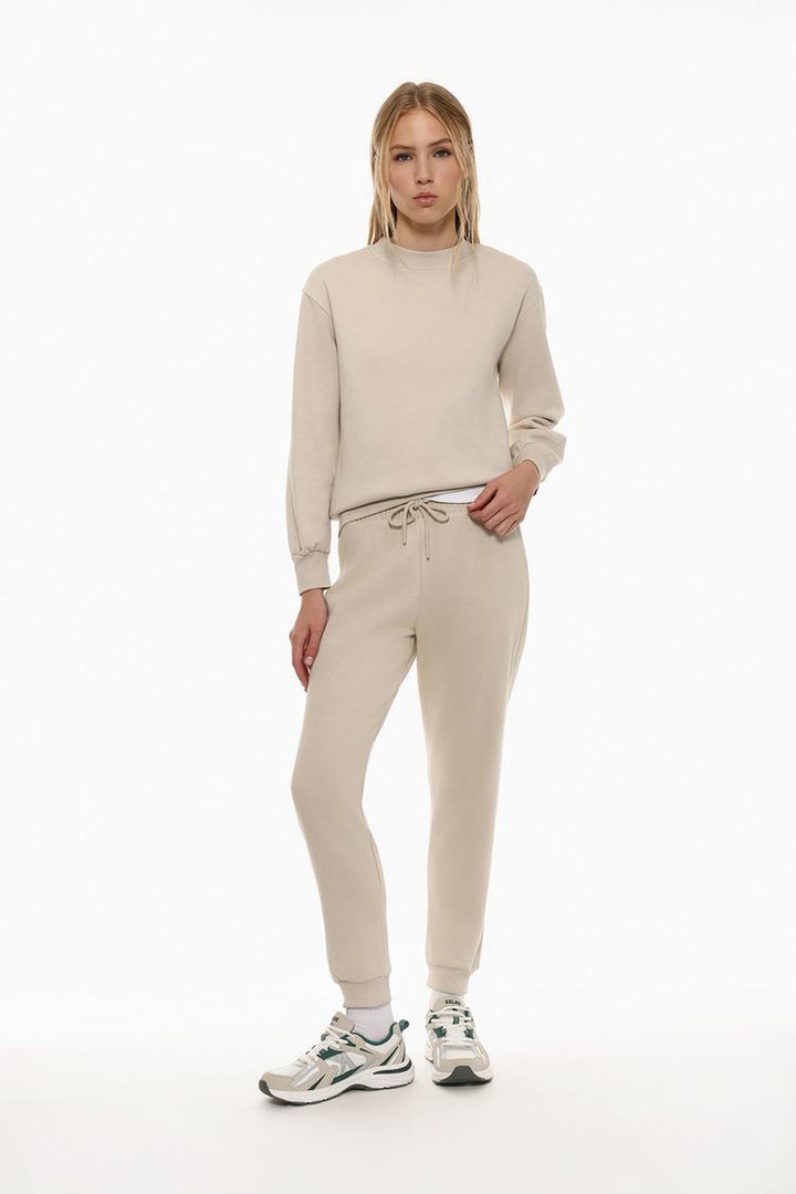 Full body view of beige tracksuit bottoms, highlighting the relaxed style.